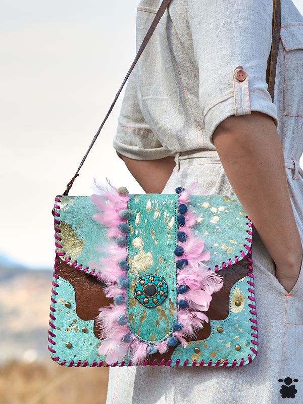 bolso-bohemio-piel-plumas-rosa olso bohemio de piel con plumas rosas y pompones multicolores, con un adorno metálico central con piedras turquesa