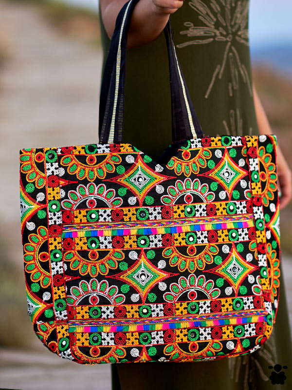 bolso-indio-floral Bolso Indio Floral con vibrantes bordados de flores en verde, rojo y amarillo sobre fondo negro, con asas negras y ribetes claros